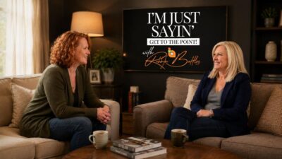 Podcast host Robbyn Battles and guest Vicki Landers sitting on cozy sofas in warm living room with real estate photo on wall, smiling and talking.